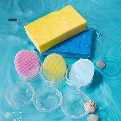 Baby shampoo brush set with soft silicone bristles in pink, yellow, and blue with clear storage cases on blue water surface with seashells