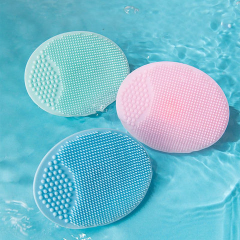 Three silicone baby shampoo brushes in pink, blue, and green floating in water with soft bristles for gentle scalp cleansing and anti-dandruff bath care.