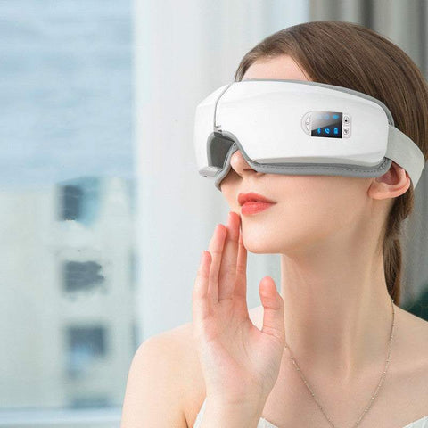 Woman using white eye massager device for relieving eye strain and reducing puffiness and dark circles
